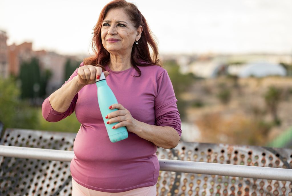 Mature hispanic woman drinking a bottle of water in a public park