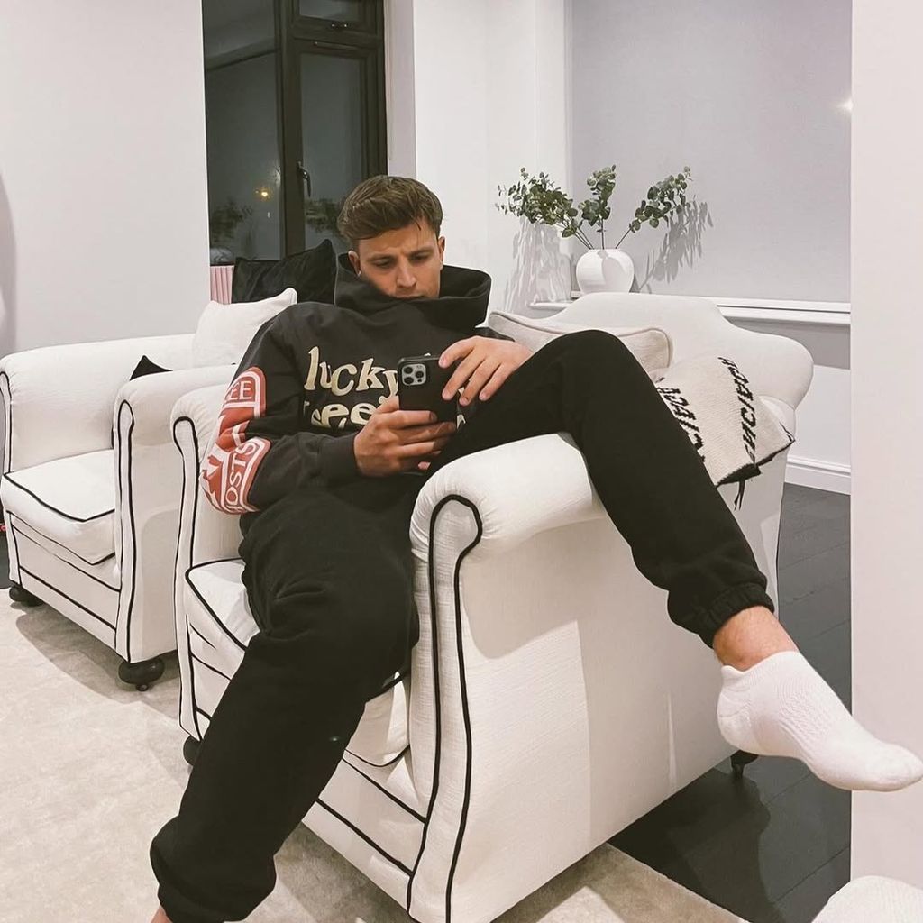 Luca sits on white armchair in living room in Brighton home