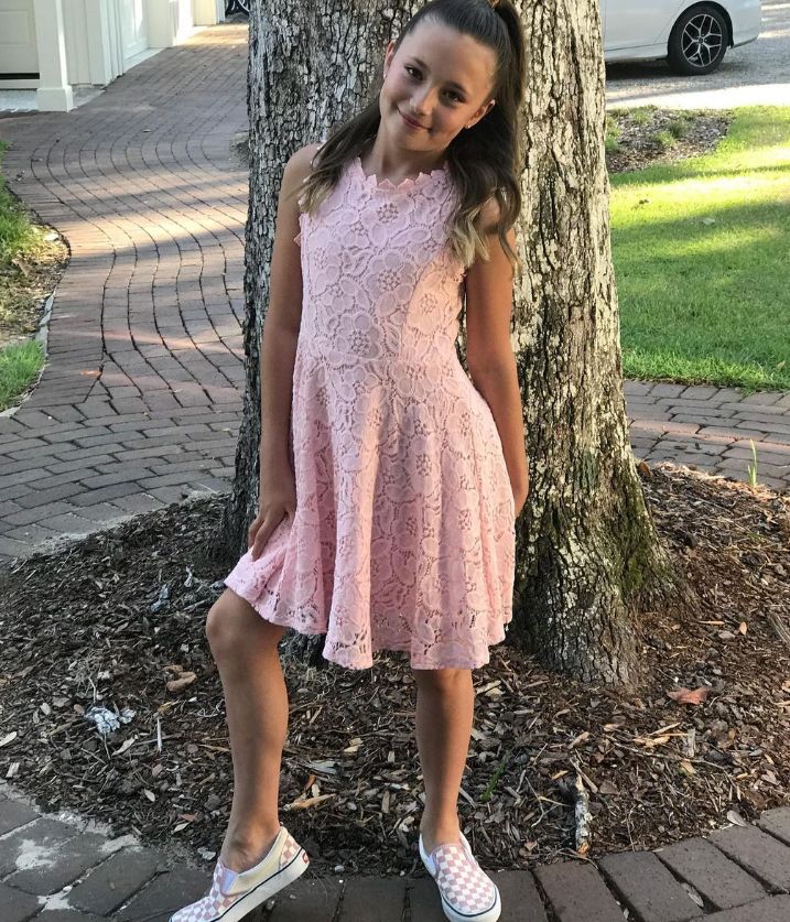 Jazmyn Bieber in a pink dress standing up against a tree