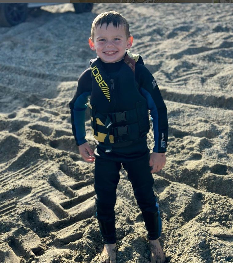 A young child on the beach in a wetsuit