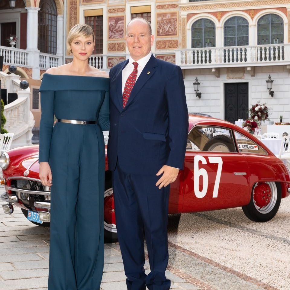 Princess Charlene in teal jumpsuit with Albert in front of vintage car