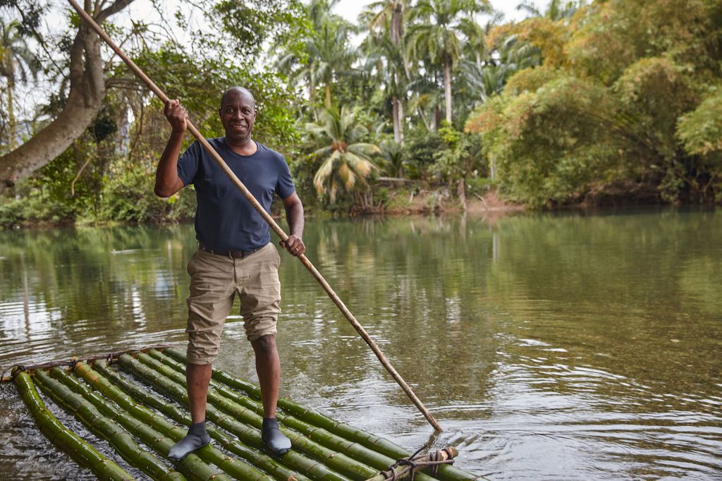 Clive Myrie stands on a water raft in a river in Cuba while filming his Caribbean Adventure TV show