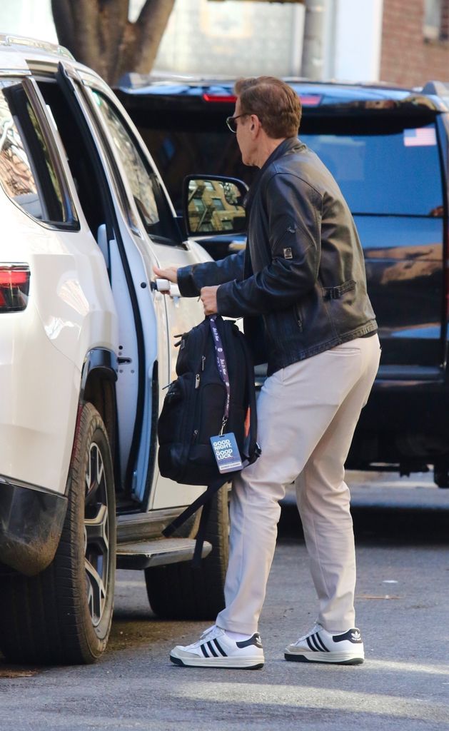 George Clooney pictured with brown hair wearing leather jacket and cream slacks in New York City 