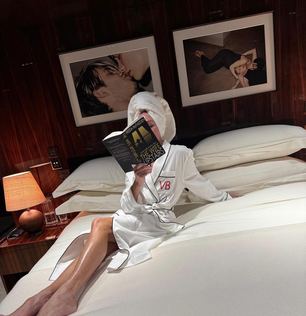 Victoria Beckham wrapped in a towel on her bed reading a book