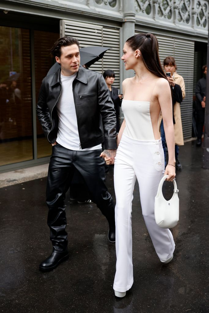 Brooklyn Beckham wears white t-shirt, black CourrÃ¨ges leather jacket, matching pants, black boots, and Nicola Peltz wears white jumpsuit with sheer details, white CourrÃ¨ges bag, outside CourrÃ¨ges,  during Womenswear Spring/Summer 2025 as part of  Paris Fashion Week on September 25, 2024 in Paris, France. (Photo by Claudio Lavenia/Getty Images)