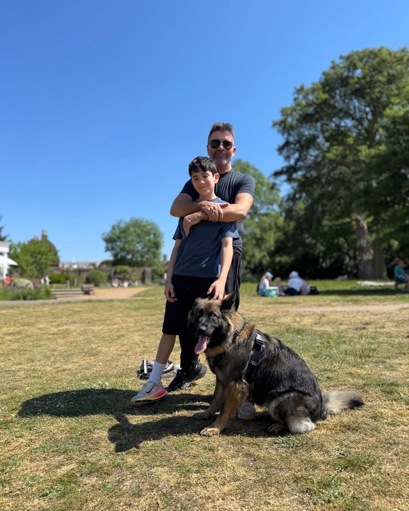 Simon Cowell wrapping his arms around son Eric while smiling for a photo with their dog sitting at their feet