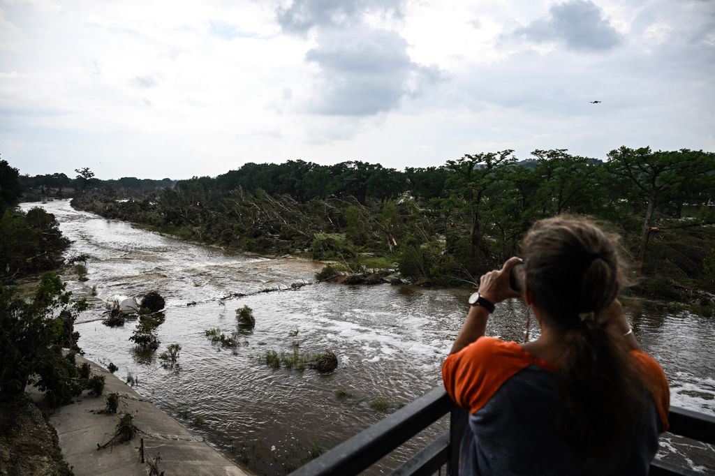 A woman takes pictures of the Guadalupe River in Kerrville, Texas, on July 6, 2025, following severe flash flooding that occured during the July 4 holiday weekend. Rescuers in Texas raced against time Sunday to find dozens of missing people, including children, swept away by flash floods that killed at least 78, as forecasters warned of new deluges. Local Texans joined forces with disaster officials to search through the night for the missing, including 27 girls from a riverside Christian summer camp