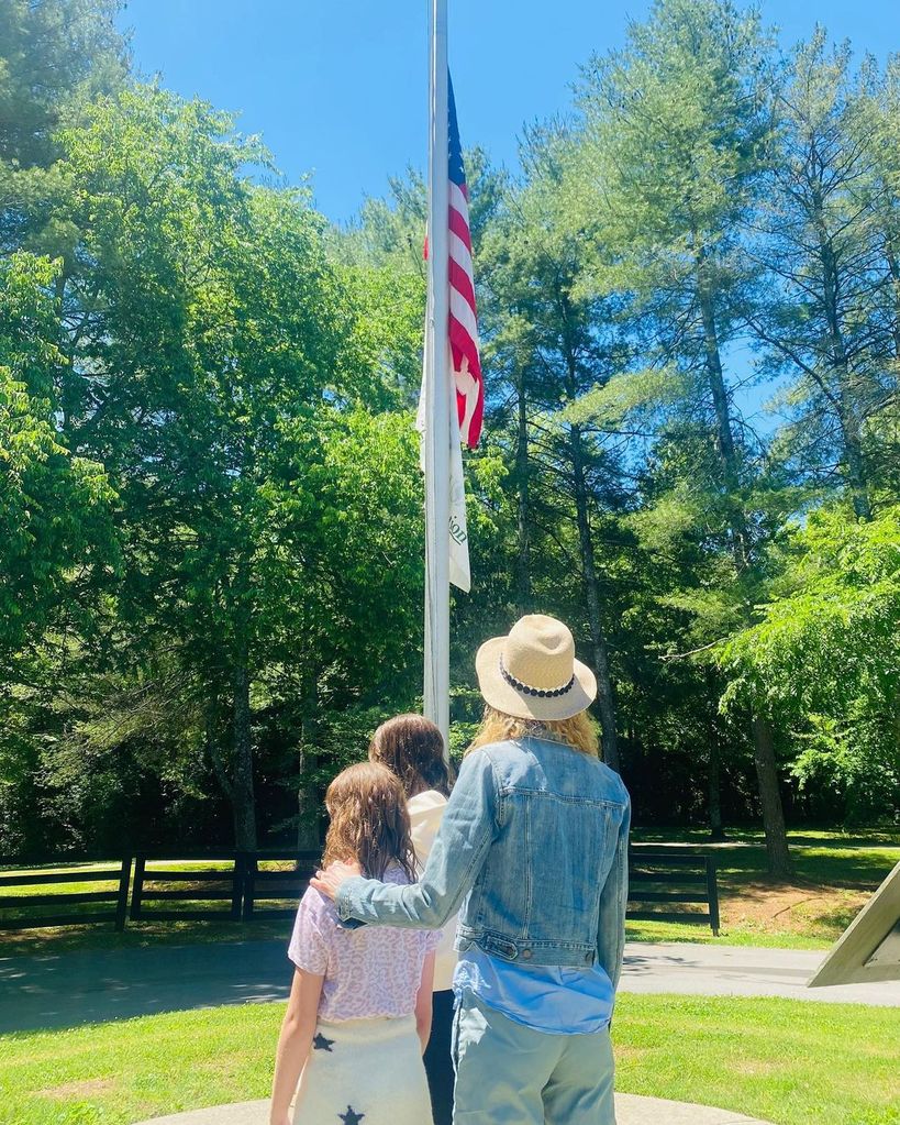 Nicole with Sunday and Faith on Memorial Day next to an American flag on a mast, their backs are at the camera