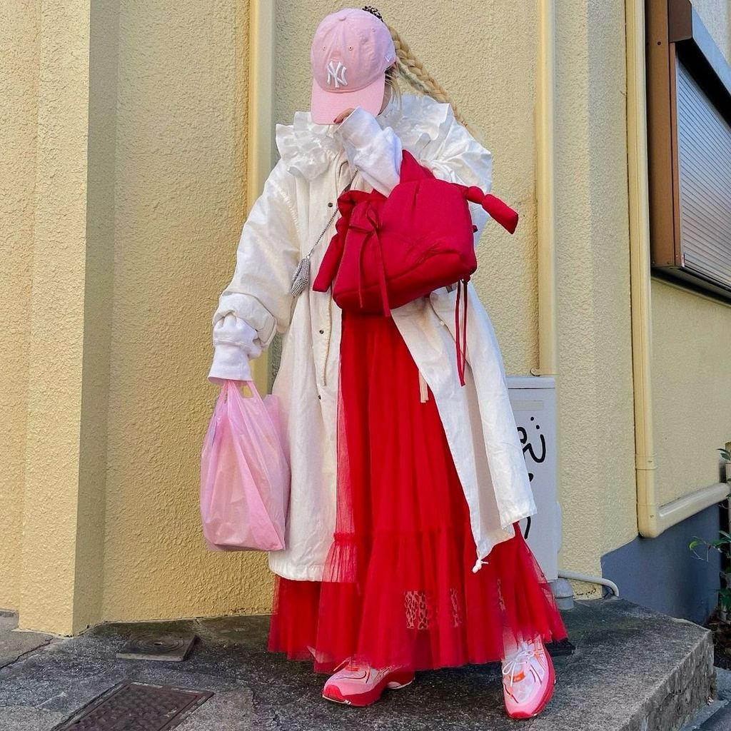 Instagram influencer @himitsu_ririan sports a coquette core outfit, wearing a red tulle skirt, pink hat and cream coloured overcoat