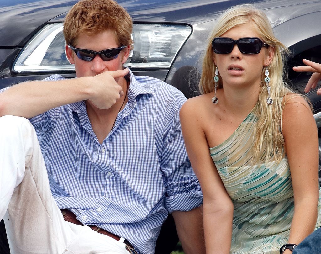 Prince Harry and Chelsy Davy sitting on the grass in front of a car wearing sunglasses