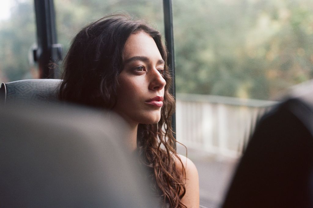 A young woman rides a bus and stares serenely out the window