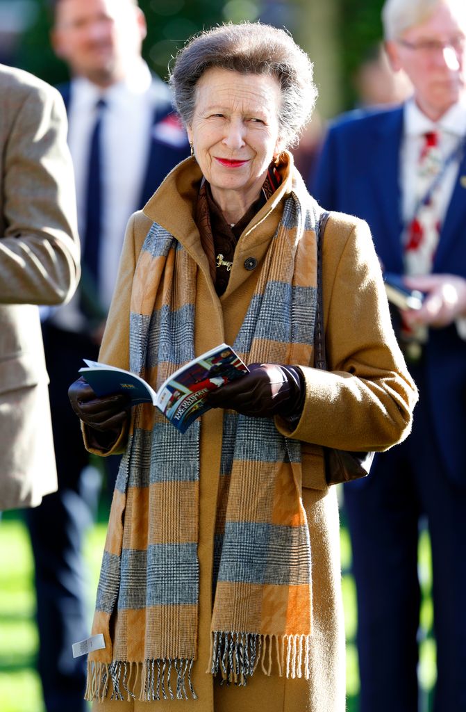 Princess Anne reading a book and smiling while wearing red lipstick