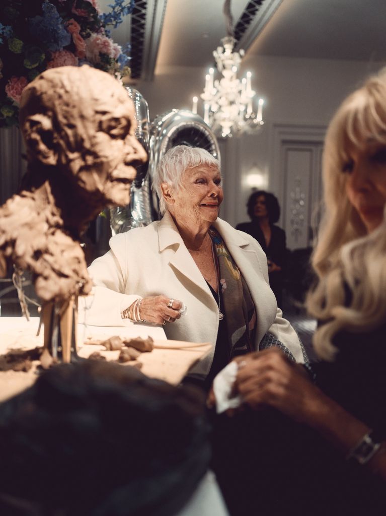 Dame Judi Dench smiling as a woman creates a sculpture of her