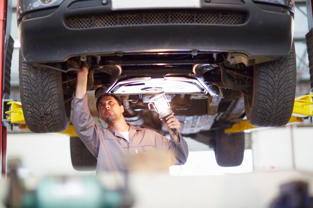 Mechanic under a car checking for pothole damage