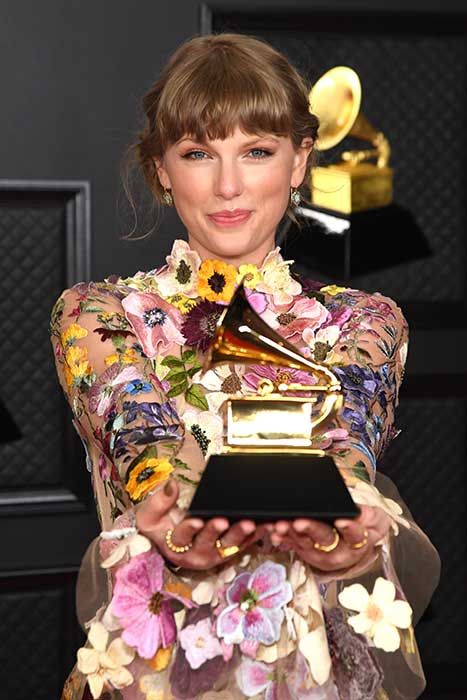 Taylor Swift smiling at the camera while holding out her Grammy