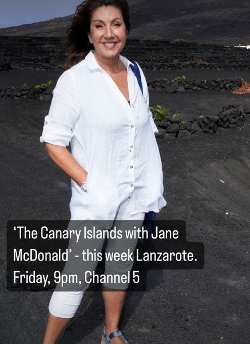 Jane McDonald in a white outfit on a black sandy beach