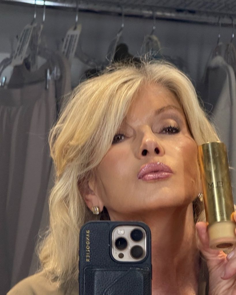 Martha posing for a mirror selfie holding up a serum to camera