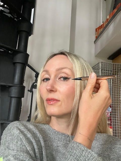 Cassie is holding a liquid eyeliner to her eye 