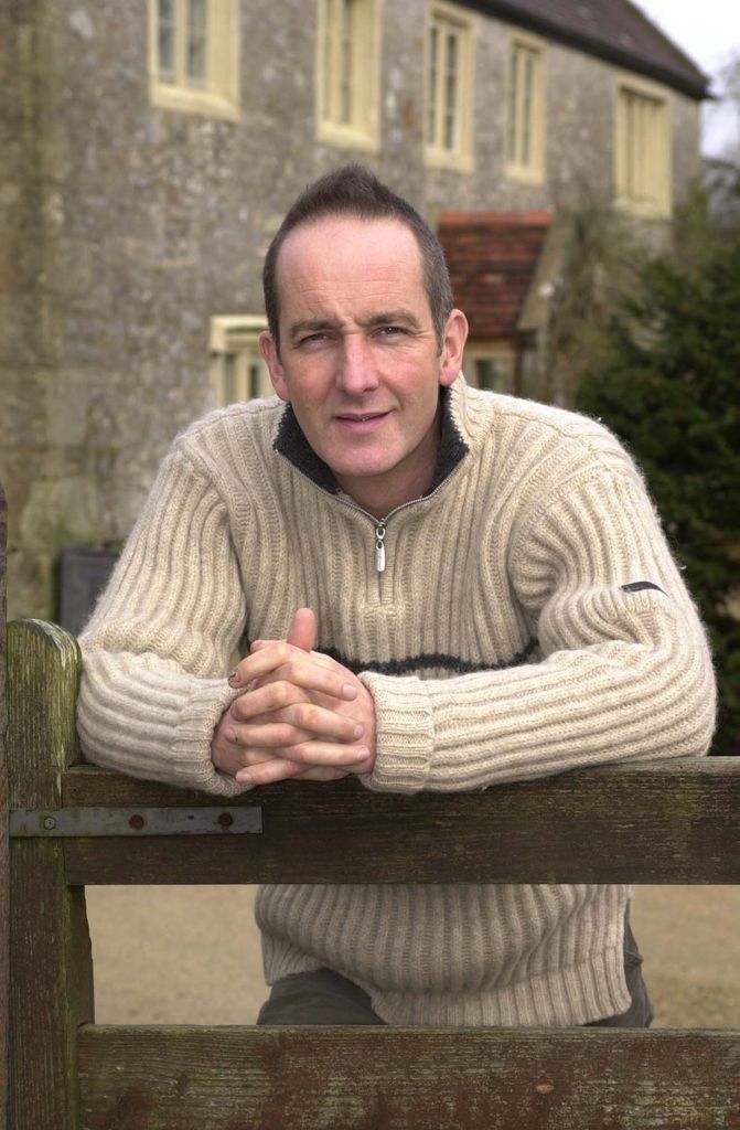 Kevin McCloud in a cream zip jumper in front of a stone home