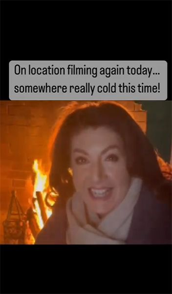 Jane McDonald sat in front of fireplace