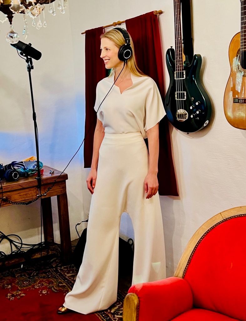 A woman dressed in white, wearing headphones, recording a song