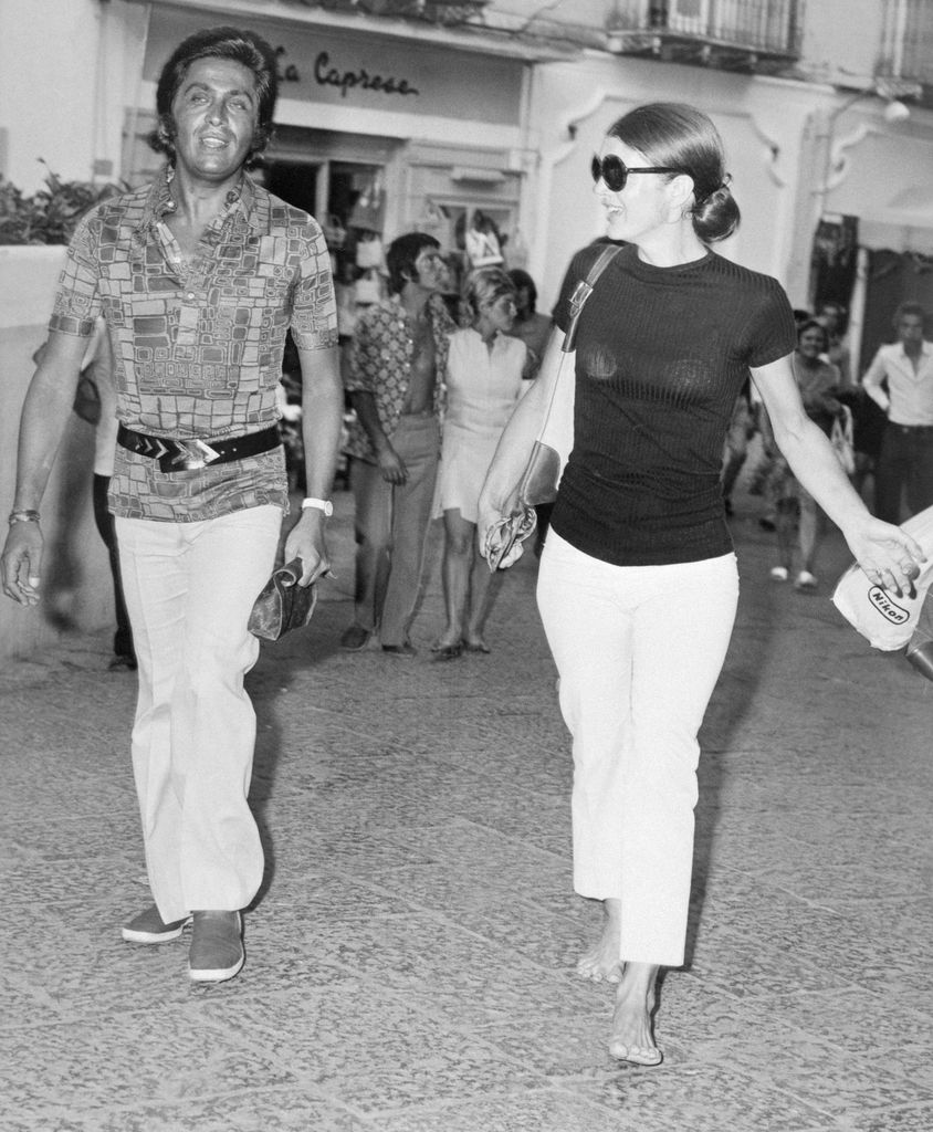 Jacqueline Onassis and Valentino walk down the street, both wearing white trousers