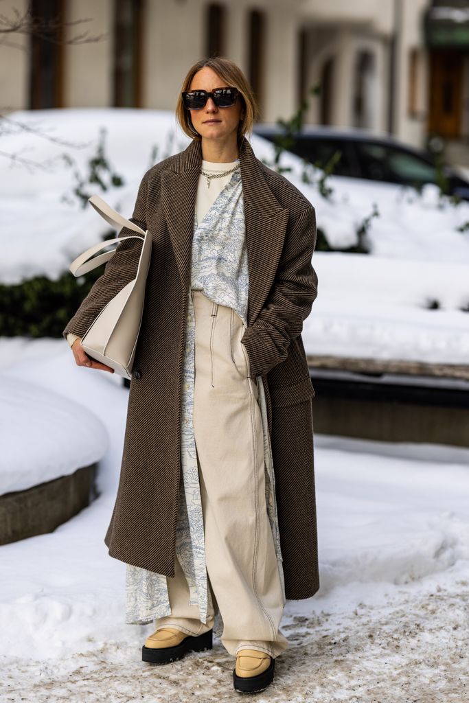 Paulina Vinter wears earthy, neutral ensemble with a mix of textures looks effortlessly cool in the snow. A long brown coat over wide-legged pants and layered with soft beige knits captures understated elegance.