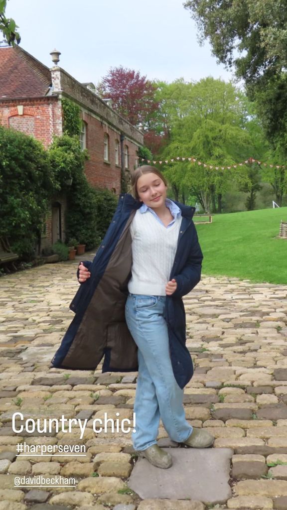 Harper Beckham wears jeans and wellies with a navy trench coat against an idyllic backgroun