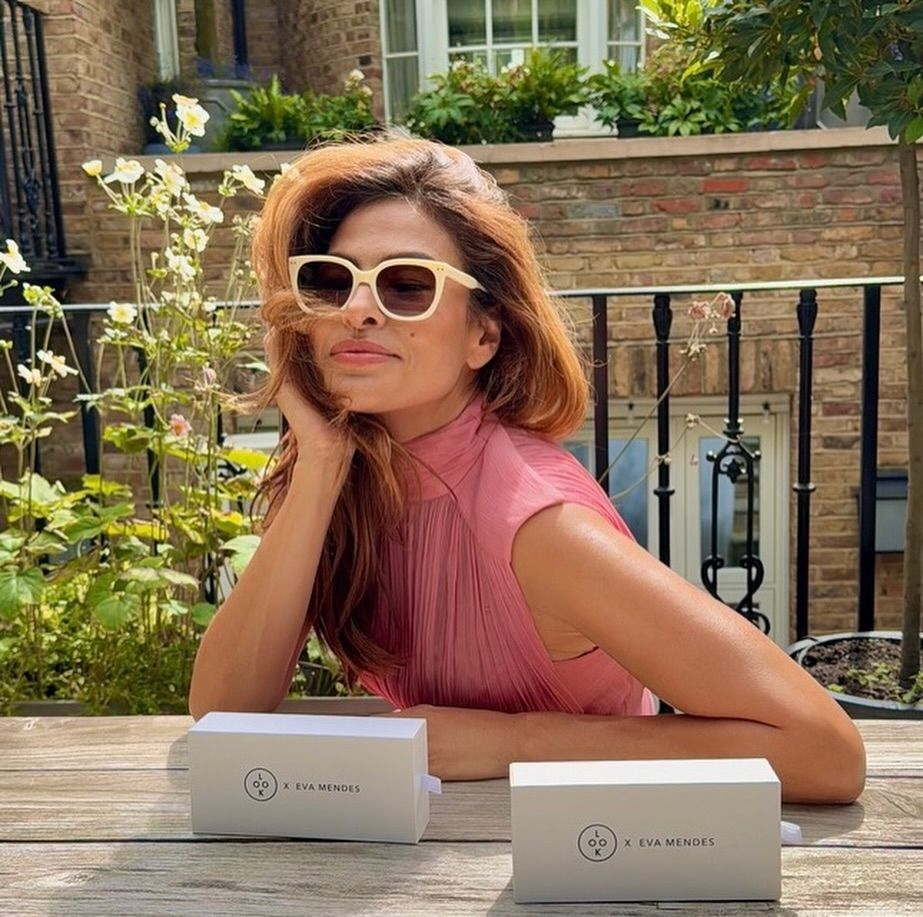 Eva Mendes sitting on a terrace in a pink dress wearing sunglasses