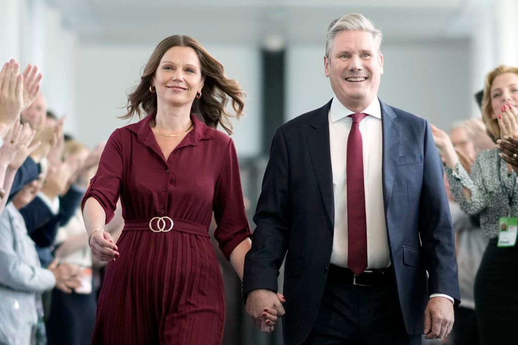 Keir Starmer holding hands with his wife Victoria, who wears a maroon dress