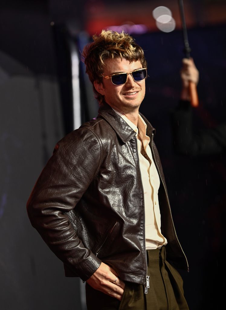 A photo of Joe Keery wearing sunglasses and a brown jacket