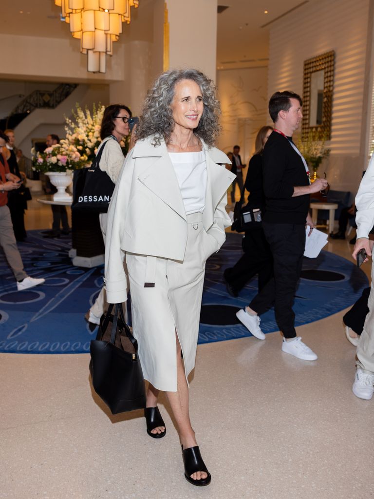 Andie MacDowell wears a light taupe cropped jacket and matching midi skirt with black mules and a black handbag