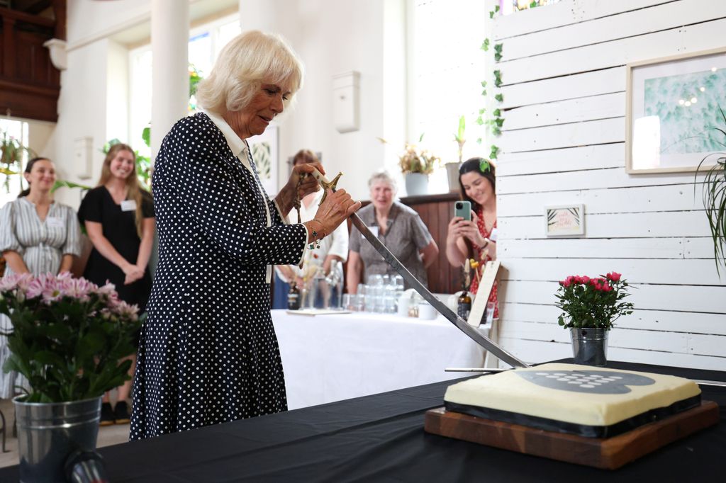Queen Camilla cuts a cake with the lord lieutenant sword as she visits community projects supported by the Cornwall Community Foundation