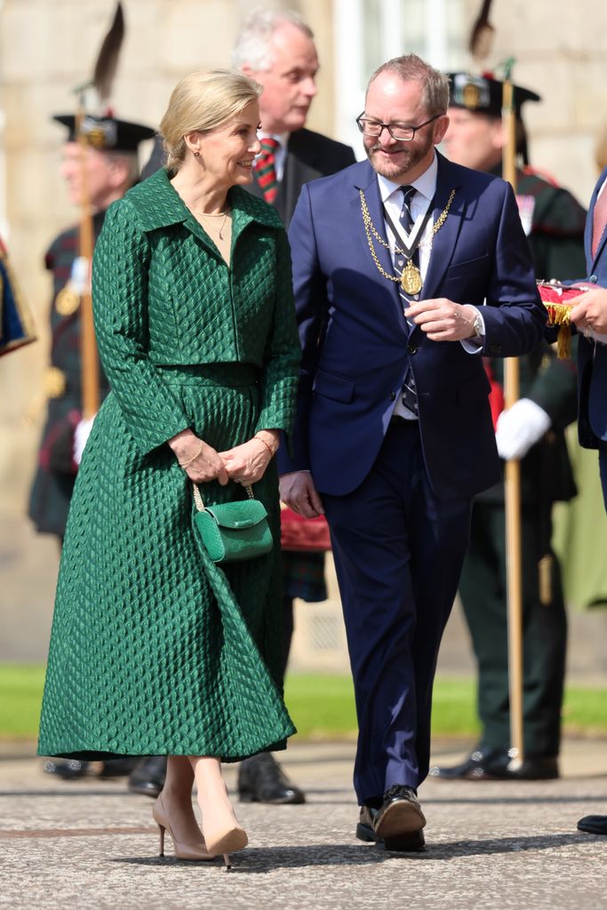 Sophie andando com look verde conversando com homem de terno