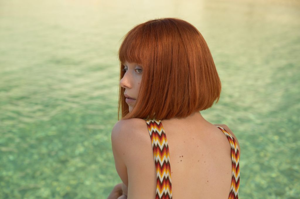 young woman with short red haircut sitting by pool
