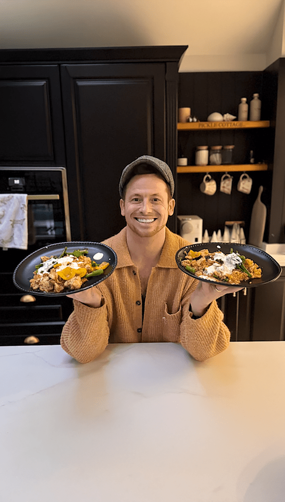 Joe Swash holding two plates of food in home kitchen