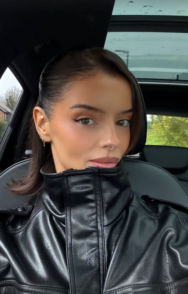 Maura Higgins in her incredible leather jacket takes a selfie in a car. Her hair is slicked back. 