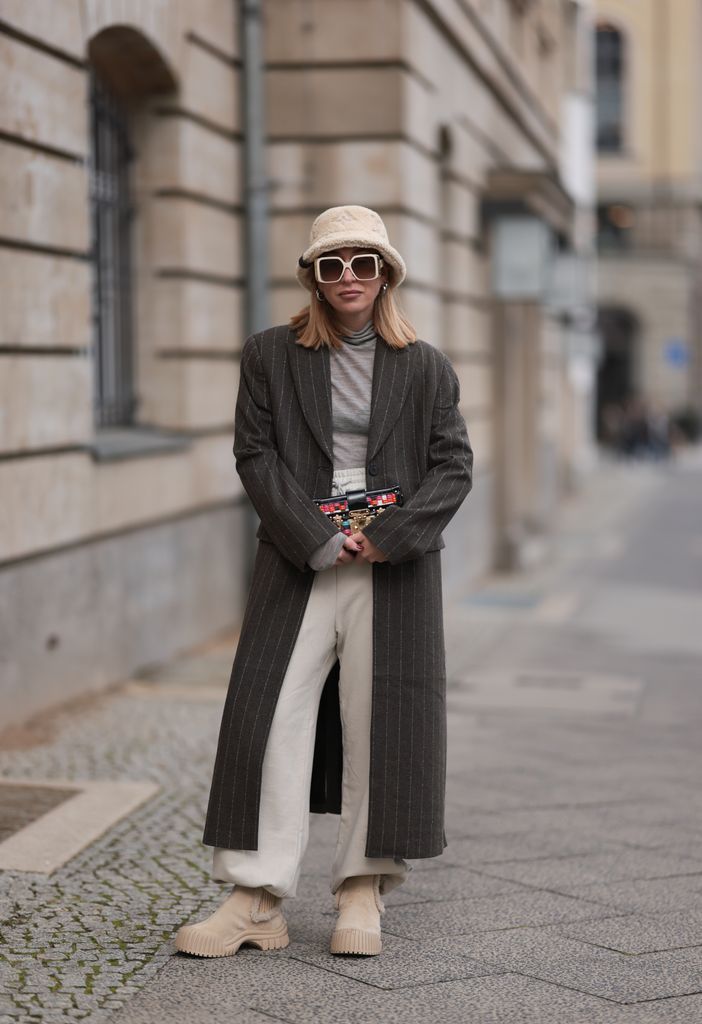 Sonia Lyson wearing a grey pinstripe coat, beige jogging bottoms, fuzzy bucket hat and sunglasses plus beige boots with chunky soles
