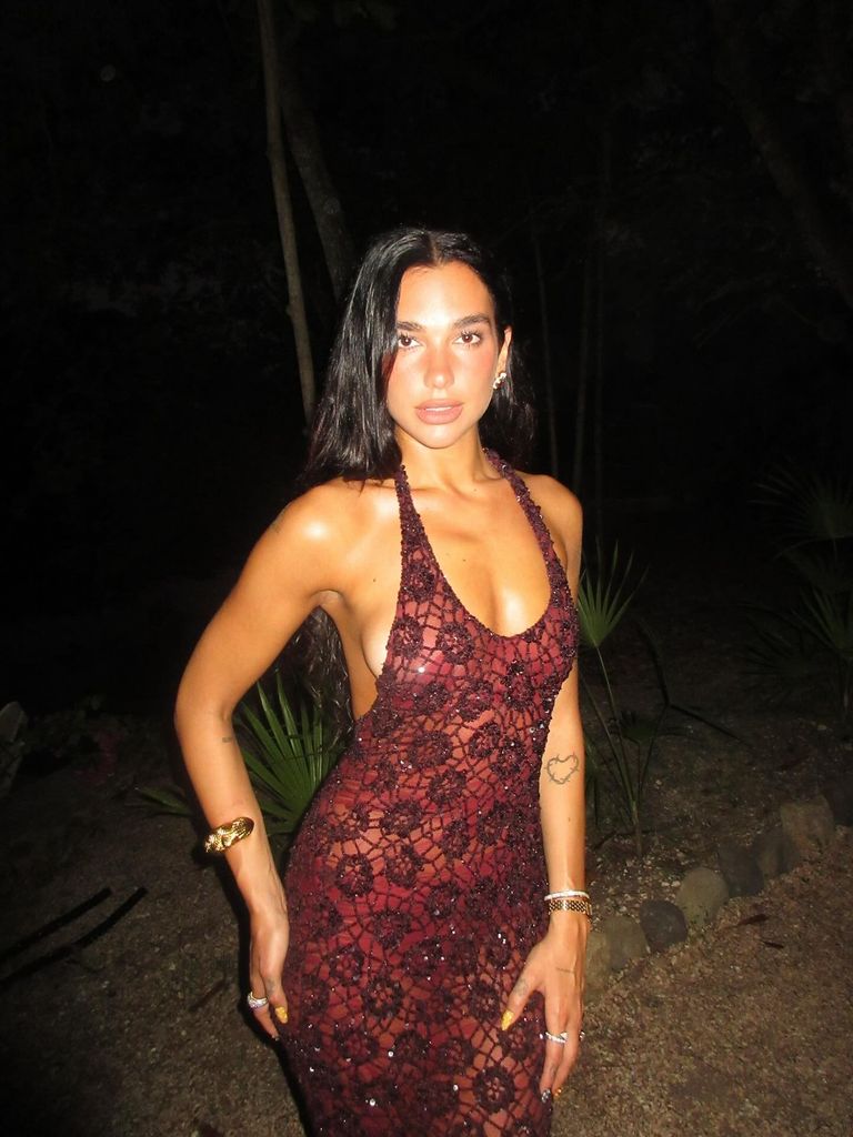 Dua Lipa poses on a beach wearing a red beaded gown