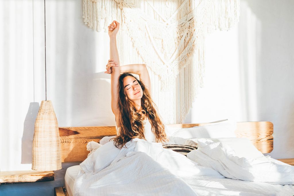 Woman relaxing on a bed. Woman stretching hands in bed.