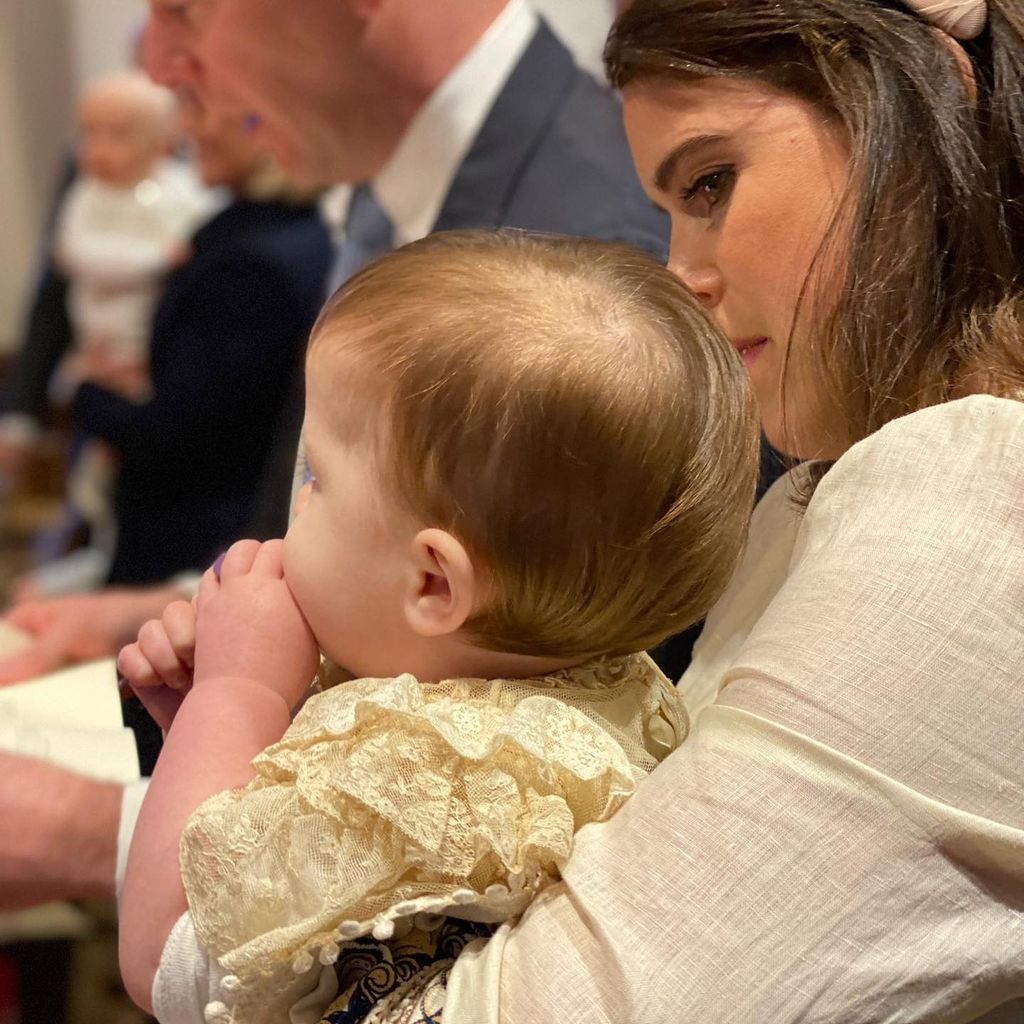 August Brooksbank wearing christening gown sitting on mother Princess Eugenie's lap
