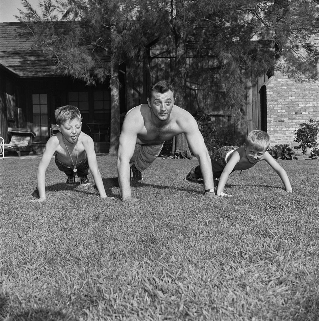 Robert Mitchum and his sons, James and Christopher, shirtless doing pushups in the garden 1951. 