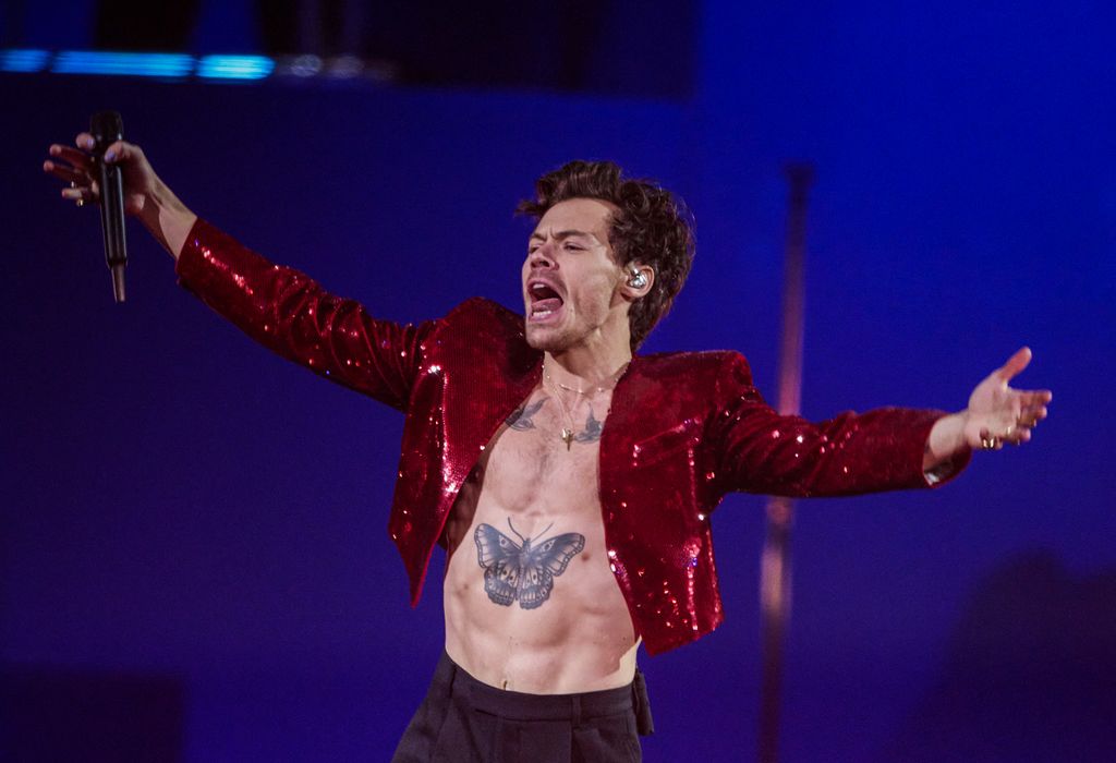 Harry on stage with arms out in red glitter jacket