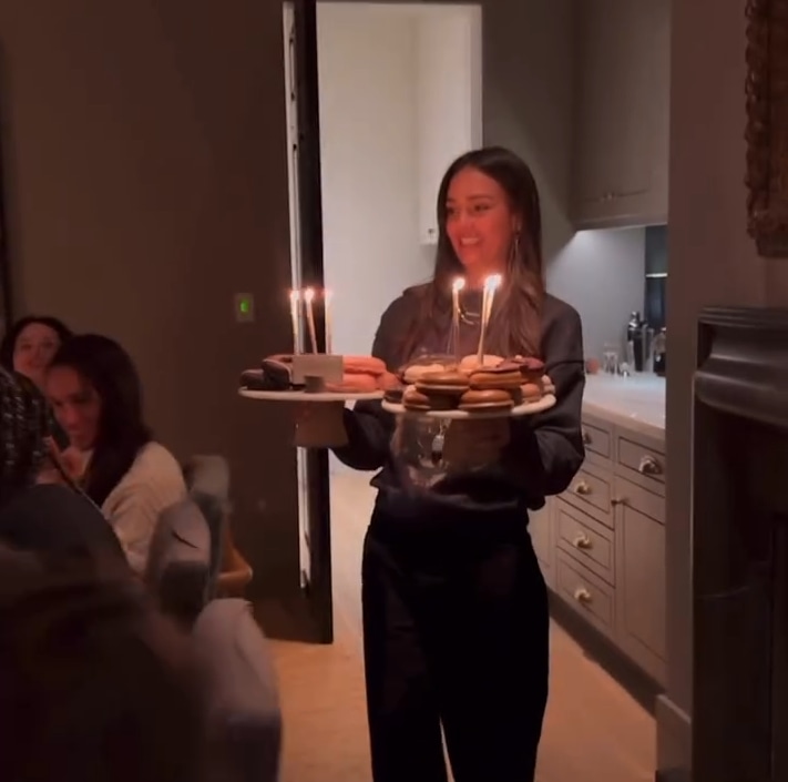 Meghan Markle can be seen sitting next to Kerry Washington as Jessica Alba carries a plate of doughnuts with lit birthday candes