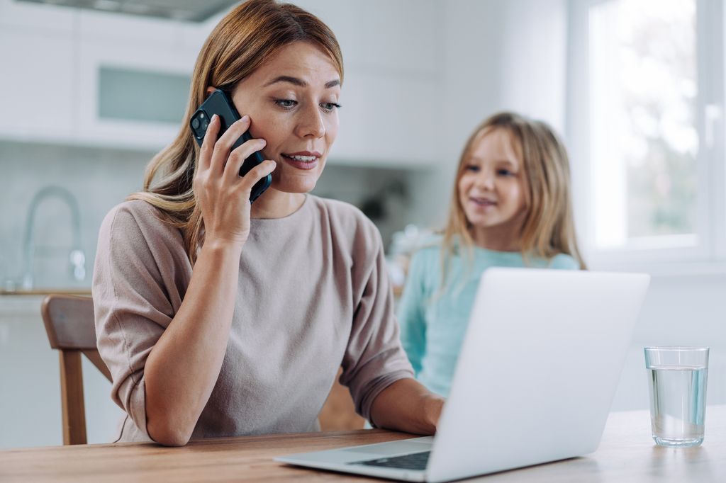 Shot of little girl distracting dedicated young businesswoman working on laptop and talking on mobile phone at home.