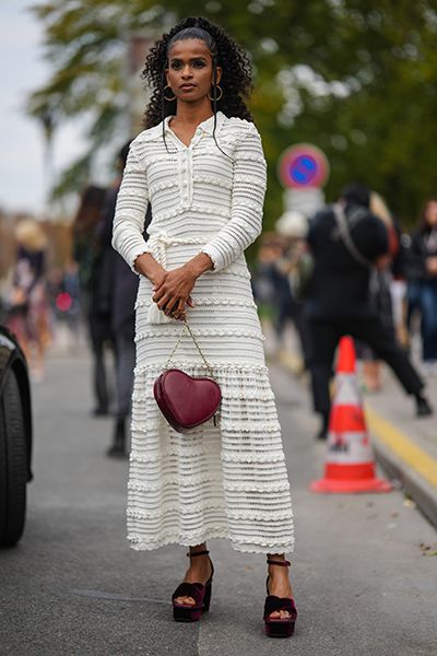 Woman wears cute outfit of white midi dress and red heart bag
