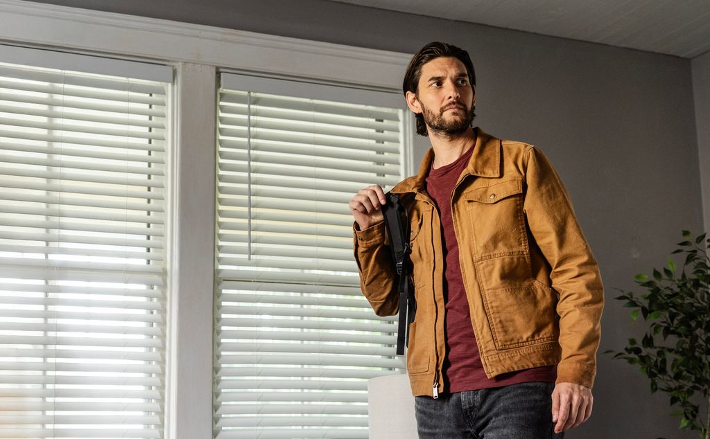 man in brown jacket and rucksack standing in house