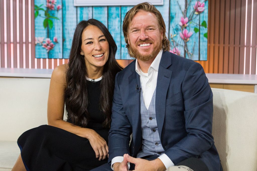 Chip Gaines in a blue suit and Joanna Gaines in a black dress smiling on TV