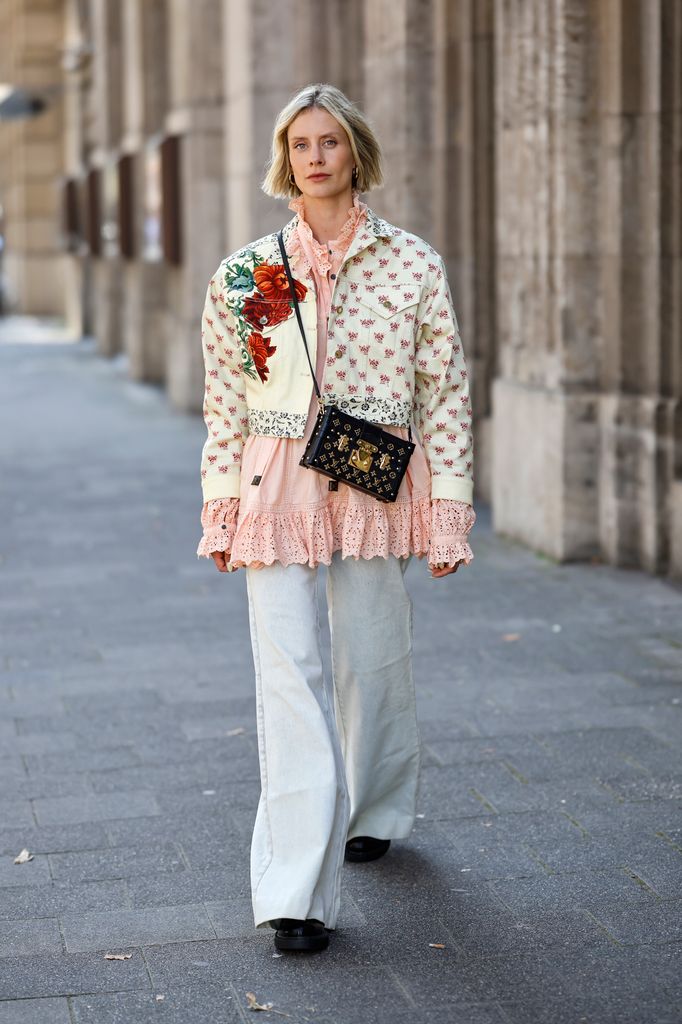  Influencer Lisa Hahnbueck wearing a mixed floral trucker jacket by Louis Vuitton, a flesh colored broderie anglaise long-sleeved babydoll blouse by Louis Vuitton, light grey wide leg pants by Louis Vuitton, a black bag with gold monogram details by Louis Vuitton and black shiny shoes by Prada seen during the Mercedes-Benz Fashion Week 