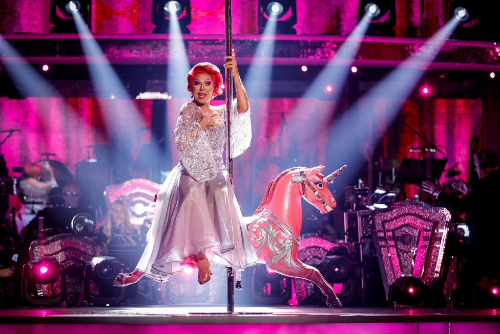 La Voix in a silver dress on a pink carousel horse